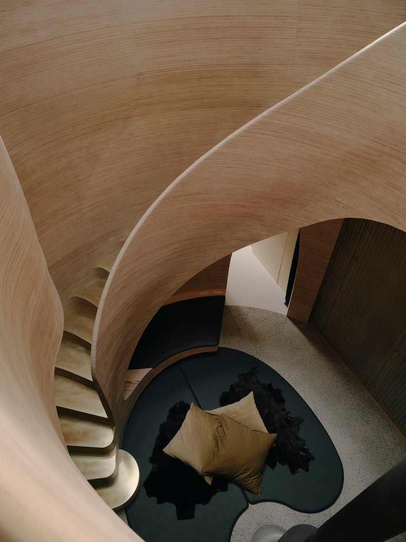Top-down view of curved timber ceiling ribs over interior space with organic sleeping platform below