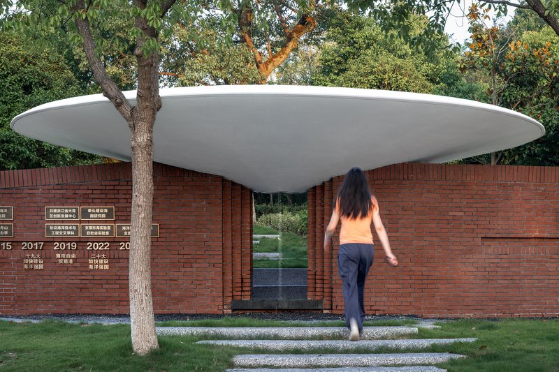 Red brick wall memorial with white disc roof canopy and visitor approaching along grass path