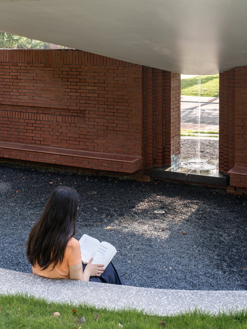 Interior courtyard with red brick walls and seated visitor reading beneath smooth white ceiling
