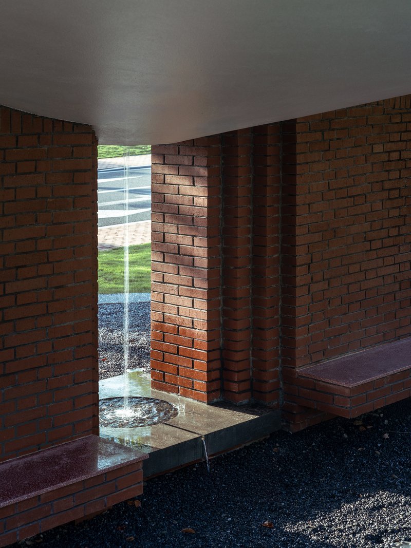 Interior view through the narrow brick opening with built-in benches and water feature beyond
