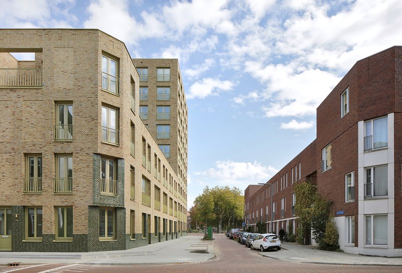 Residential street lined with buff brick housing blocks and parked cars under scattered clouds