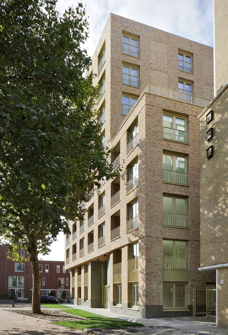 Street elevation of a buff brick housing block framed by mature trees in summer foliage
