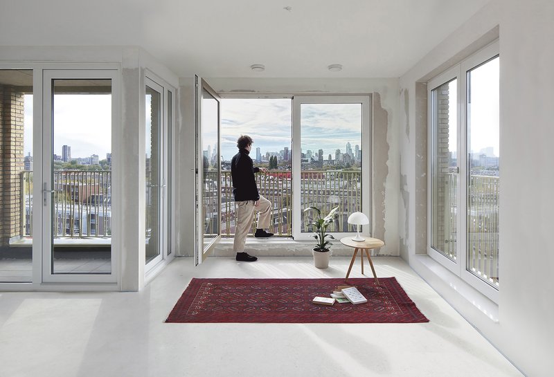 White interior room with floor-to-ceiling windows opening to a balcony overlooking the cityscape