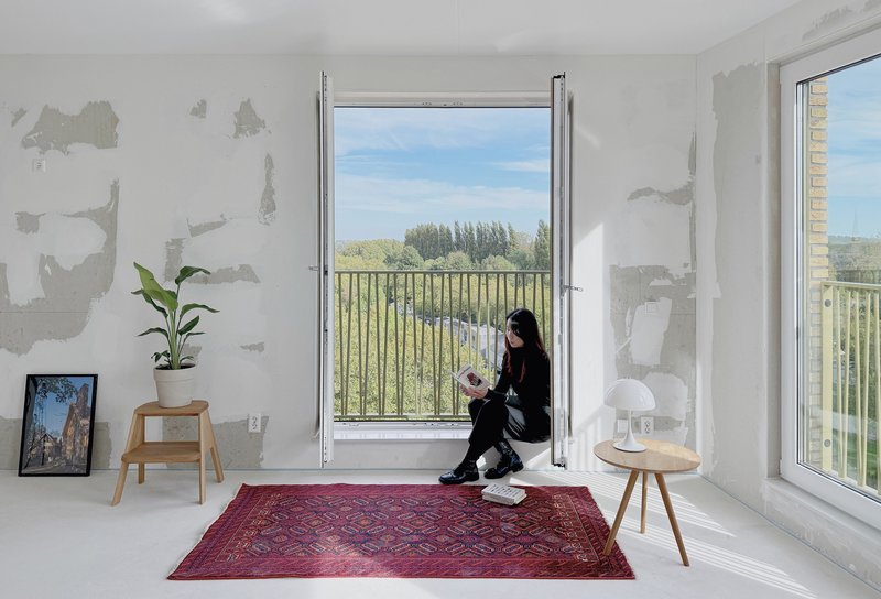 Person seated in the window threshold reading as sunlight streams across unfinished plaster walls