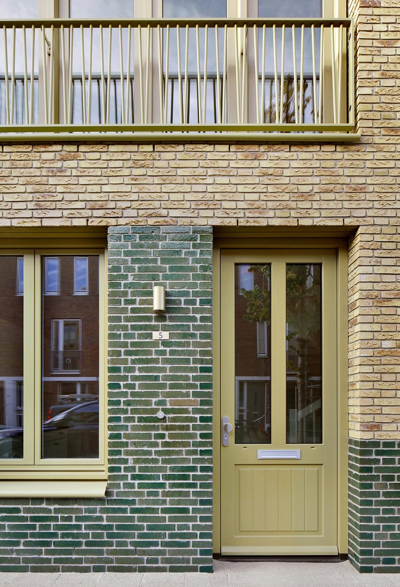 Ground floor entrance with pale yellow door framed by green glazed brick and buff brick