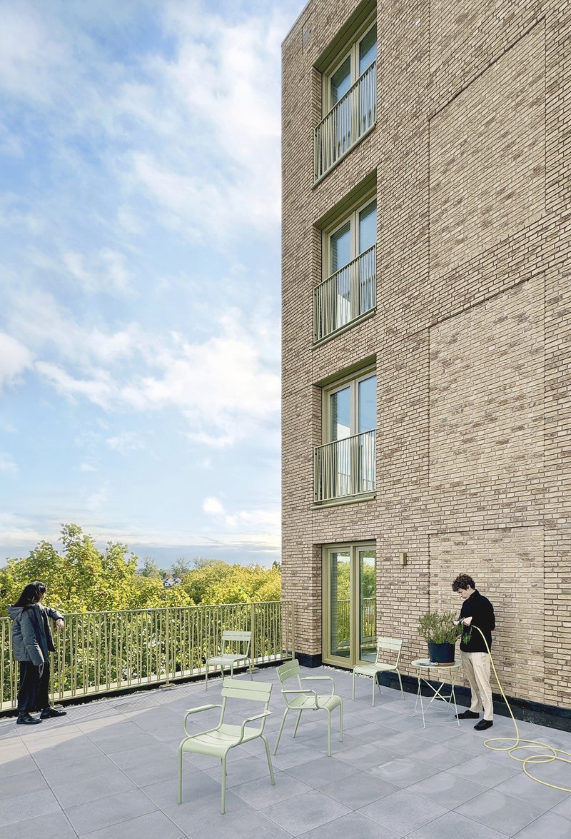Shared terrace against the brick tower with pale green chairs and residents in afternoon light