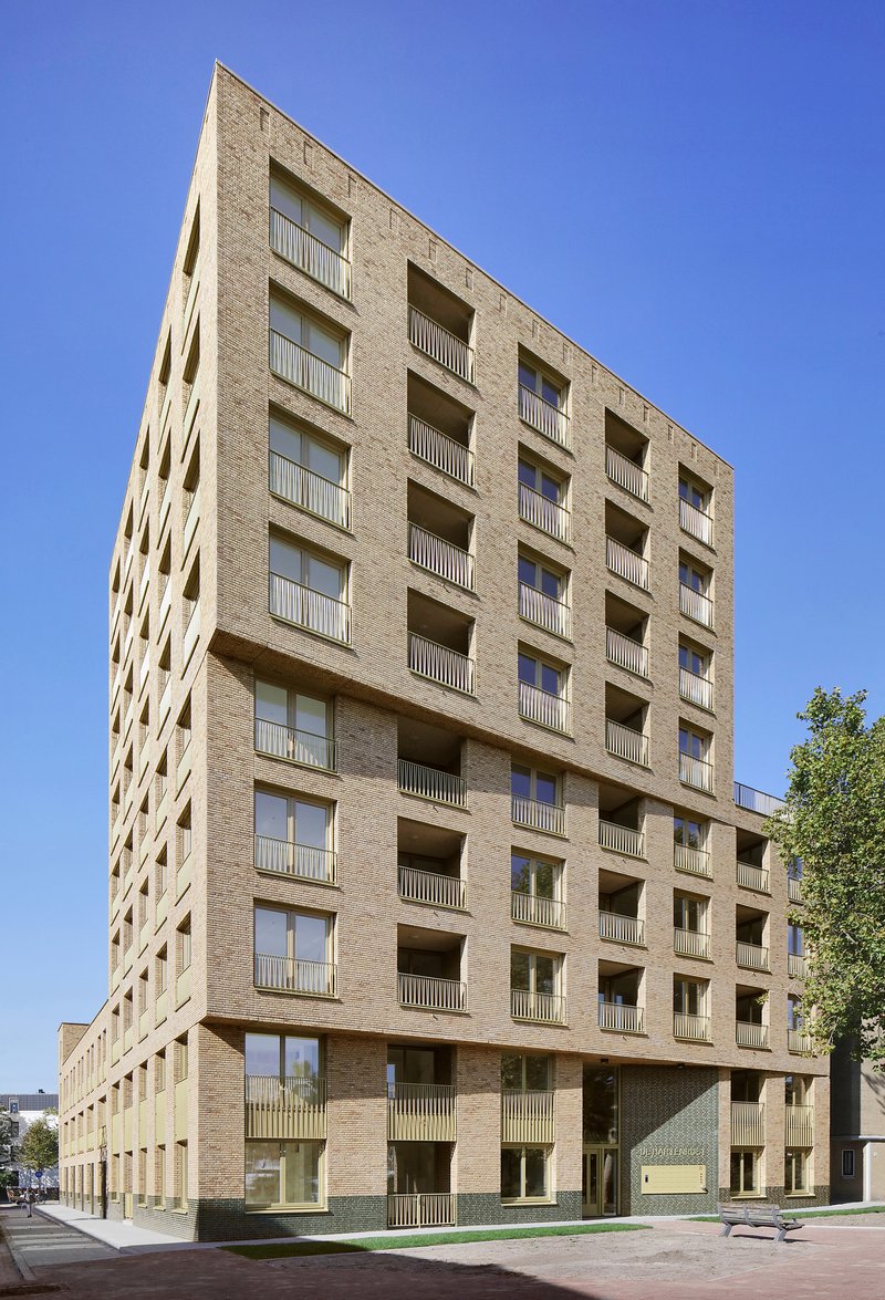 Full elevation of the brick residential block with recessed balconies under a clear blue sky