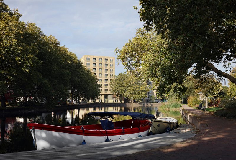 Residential tower viewed across a canal with moored boats and overhanging tree branches