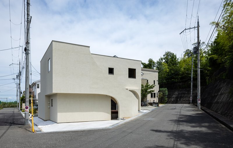 Corner facade with arched recesses at the base and punched square windows above on a sloped street