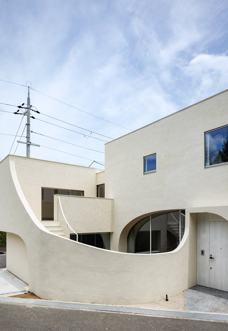 Curving exterior staircase rising between stucco volumes with utility wires crossing overhead
