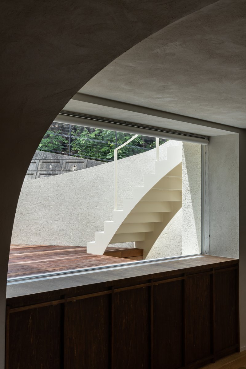 Interior view through arched opening to exterior staircase and planted hillside beyond