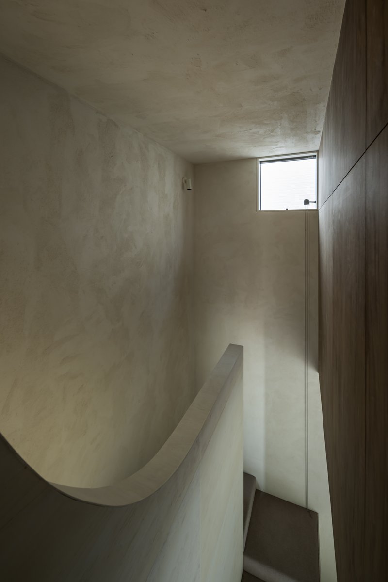 Curved plaster stairwell with dark timber wall and narrow horizontal window casting daylight