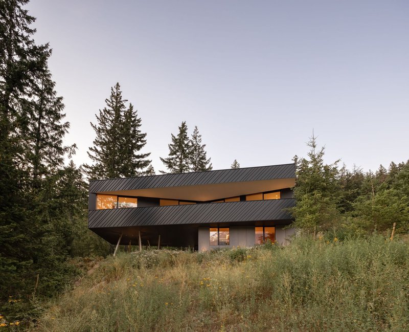 Exterior view of the cantilevered upper level with diagonal metal cladding at dusk with interior lights on