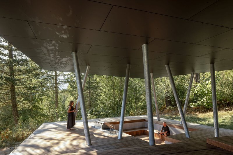 Covered timber deck supported by angled steel columns casting dappled shadows beneath the cantilevered volume