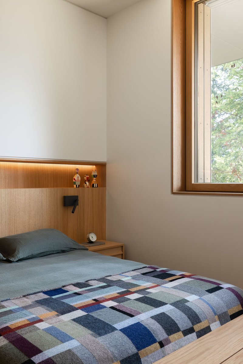 Bedroom with integrated timber headboard, reading light, and wood-framed window overlooking trees