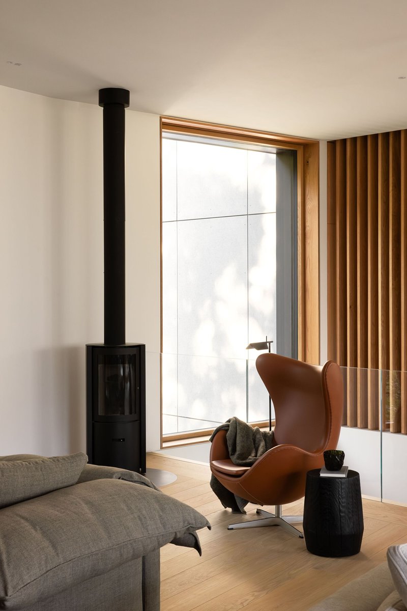 Corner reading nook with freestanding black stove, timber-framed window and leather lounge chair