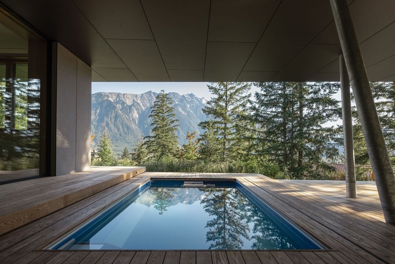 Covered timber deck with sunken pool framing a view of forested mountains beyond steel columns