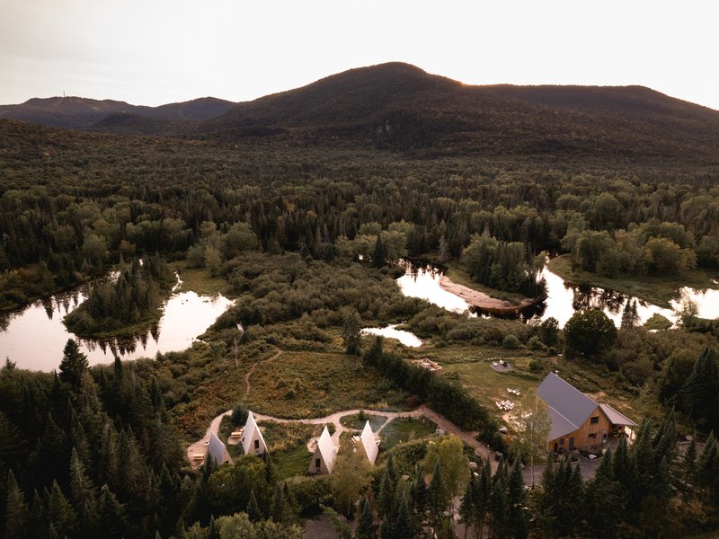 Aerial view of clustered A-frame cabins on a wooded peninsula between meandering river channels and forested hills
