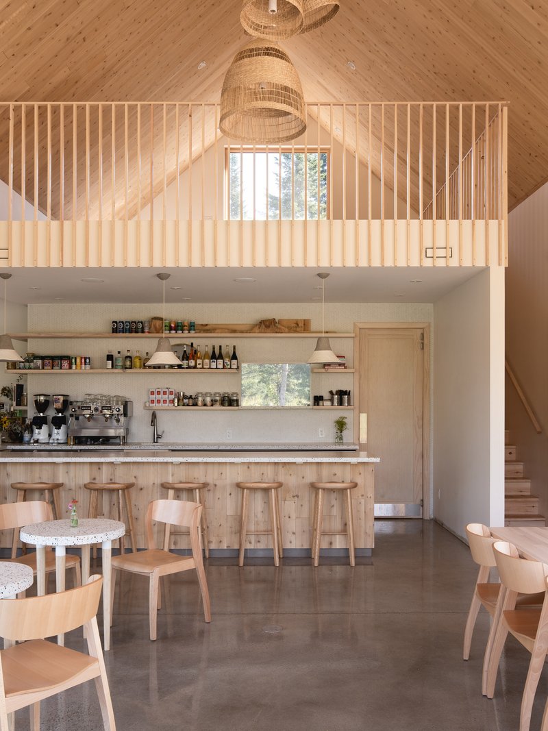 Double-height cafe interior with vertical timber slat mezzanine railing and woven pendant light above bar seating