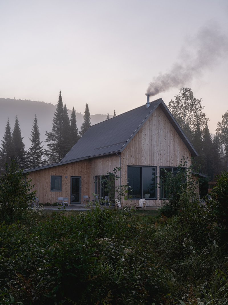 Timber-clad gable roof cabin with chimney smoke rising into the misty mountain forest at dawn