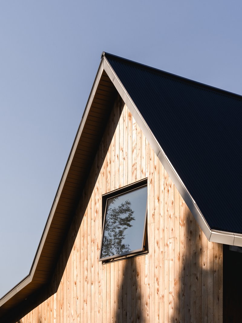 Steep gabled facade clad in vertical timber boards with square window beneath dark metal roof