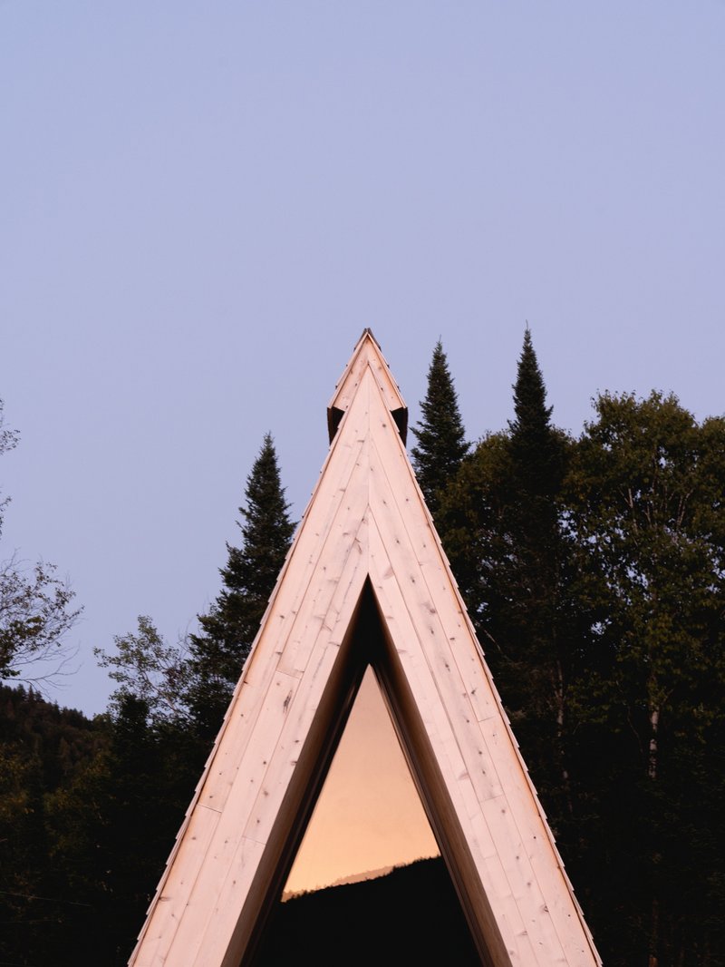 Tall triangular timber frame portal set against dusk sky and darkening conifer treeline