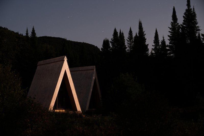 A-frame structure with cedar shingle roof and timber columns nestled among conifers at twilight