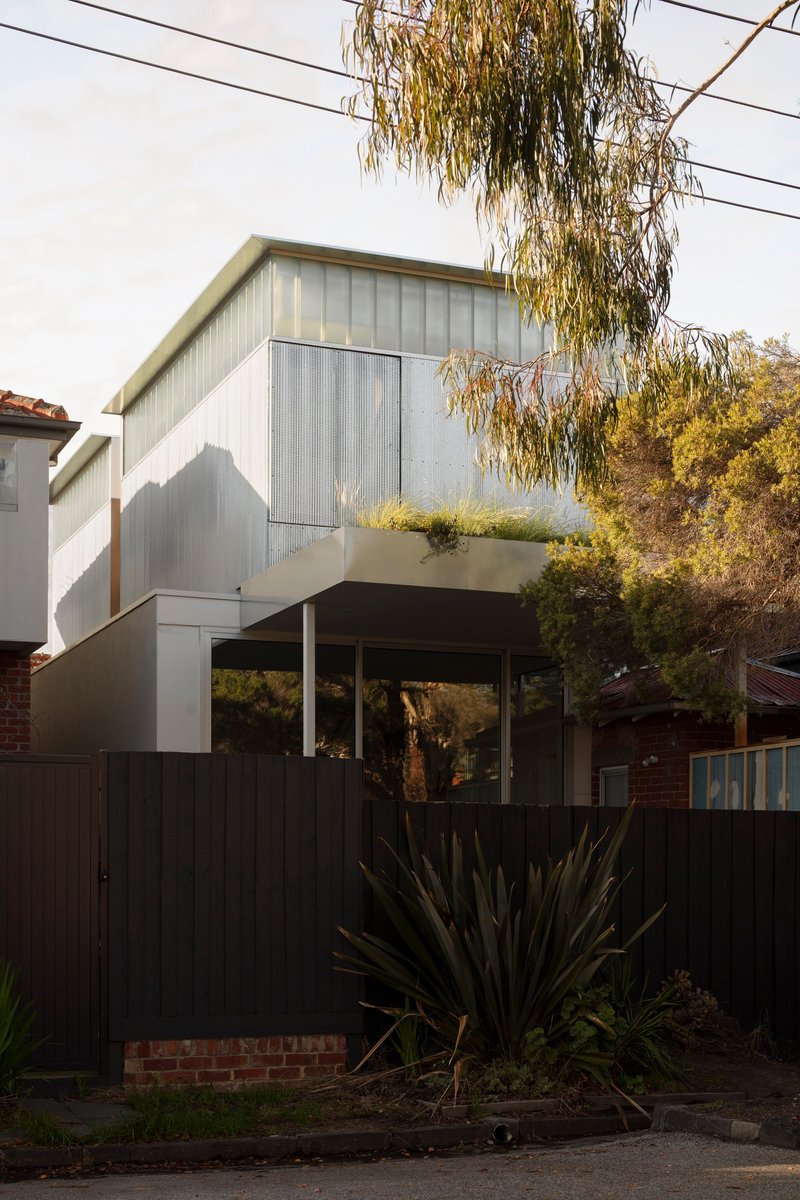 Upper volume clad in vertical metal sheeting with cantilevered terrace and planted bed beneath overhanging willow branches