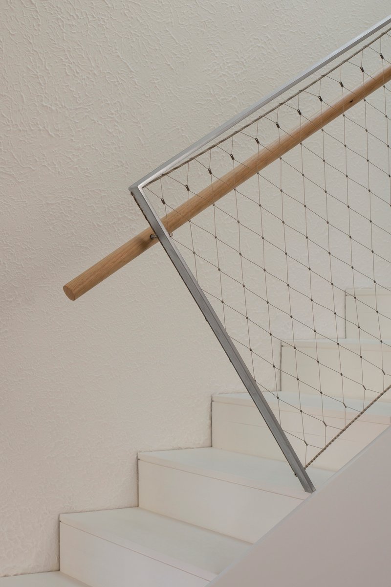 White stair with timber handrail and steel mesh balustrade against a textured plaster wall