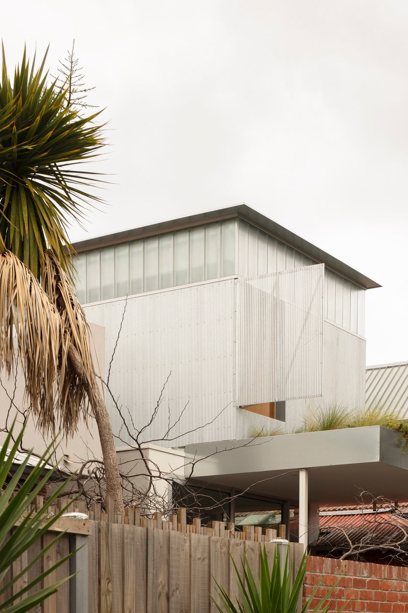 Street view of the corrugated metal facade raised on pilotis with palm trees framing the composition