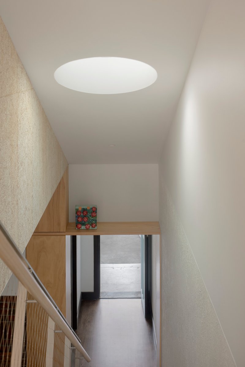 Upper level hallway with circular skylight above textured plaster walls and timber handrail