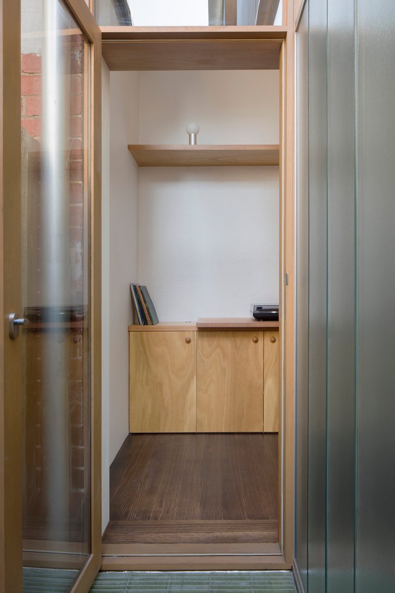View through galvanized metal door frame into timber-lined alcove with built-in shelving and cabinets