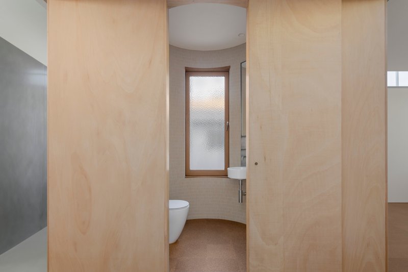 Curved bathroom wall clad in light plywood panels with translucent glass door at center