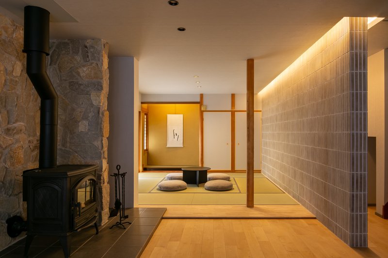View through living space to tatami room with floor cushions, stone fireplace and backlit grey tile wall