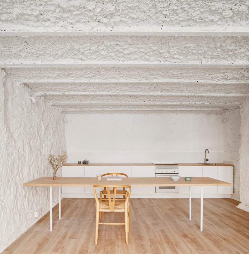 Kitchen with white base cabinets, timber countertop and dining table beneath whitewashed vaulted ceiling with exposed beams
