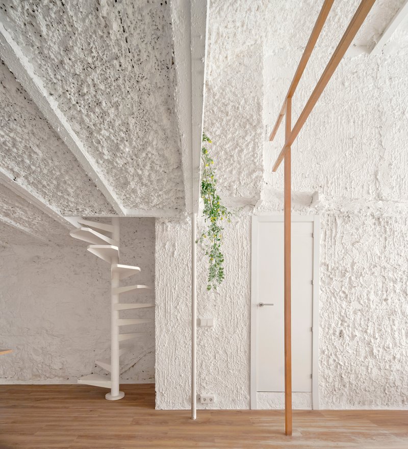 White spiral staircase beside timber structural columns and textured masonry walls with trailing greenery