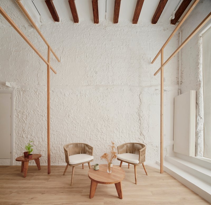 Seating area beneath exposed timber ceiling beams with textured white plaster walls and a tall window