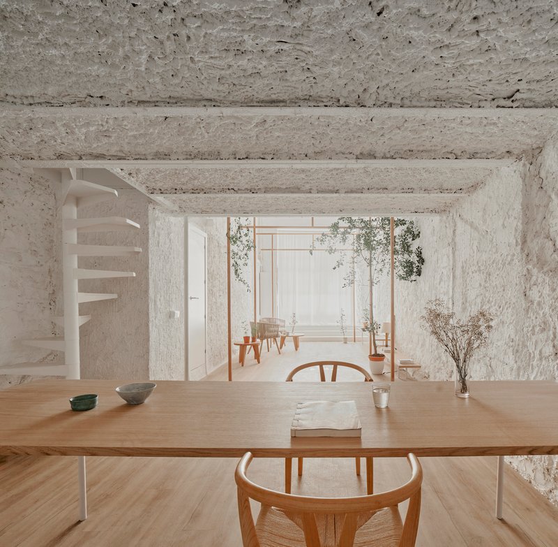 View across dining table toward spiral stair and timber pergola with potted plants in soft daylight