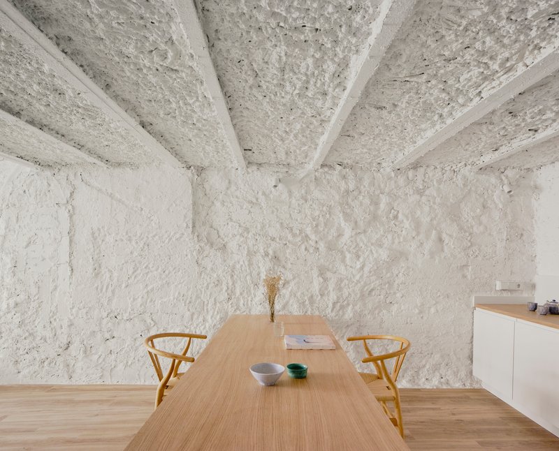 Corner of dining space with exposed structural ceiling and rough white plaster walls