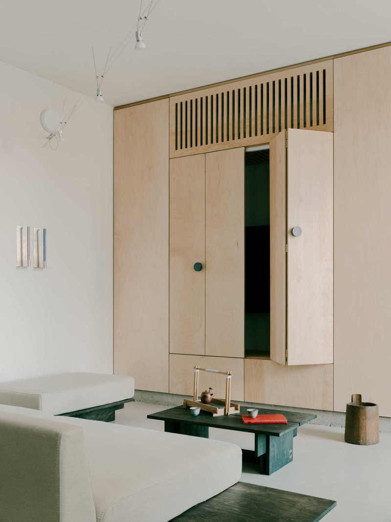 Built-in plywood storage wall with vertical slatted ventilation panel above hinged cabinet doors