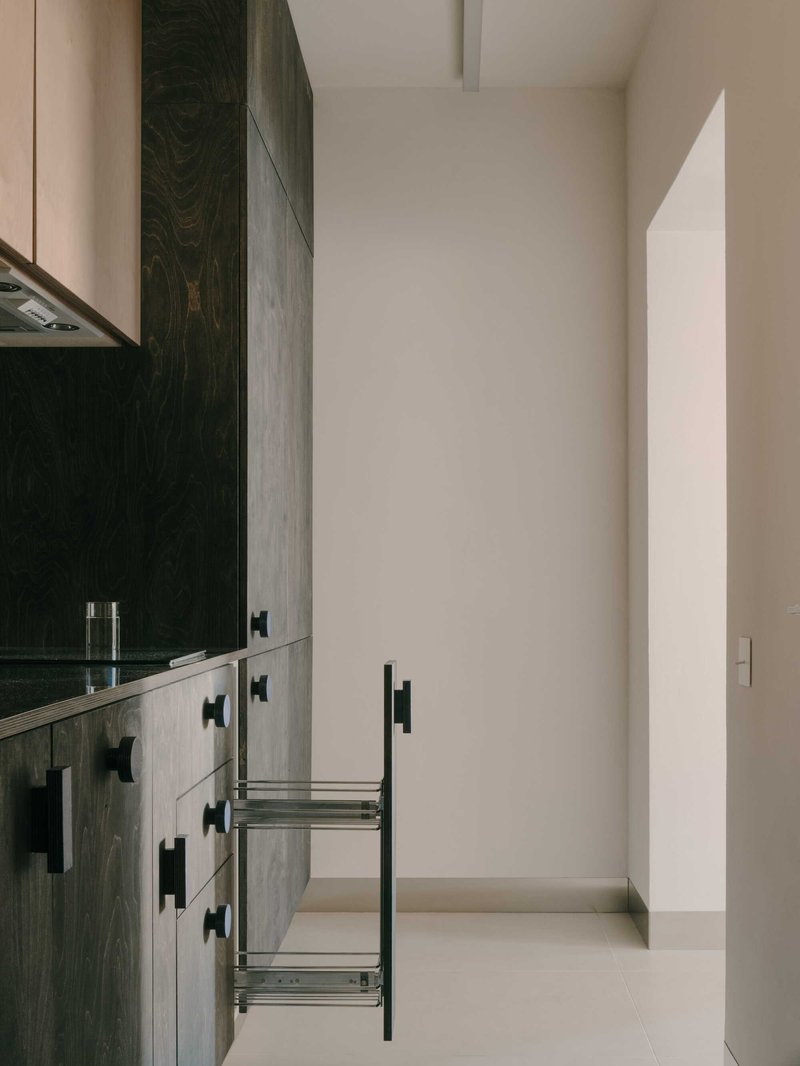 Narrow kitchen with dark wood base cabinets, black bar pulls, and open pull-out wire storage basket
