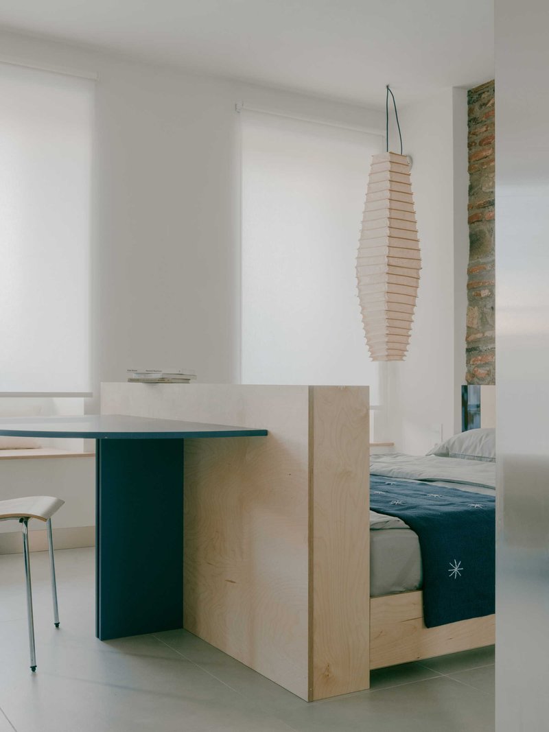 Plywood sleeping platform with green base and paper lantern pendant in a white interior