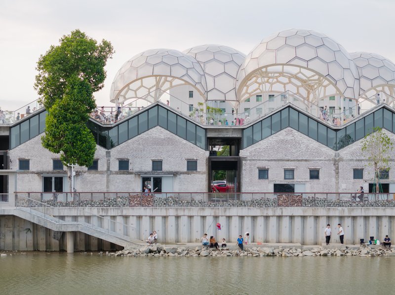 Riverfront elevation showing hexagonal geodesic domes above a concrete retaining wall with people gathered along the water's edge