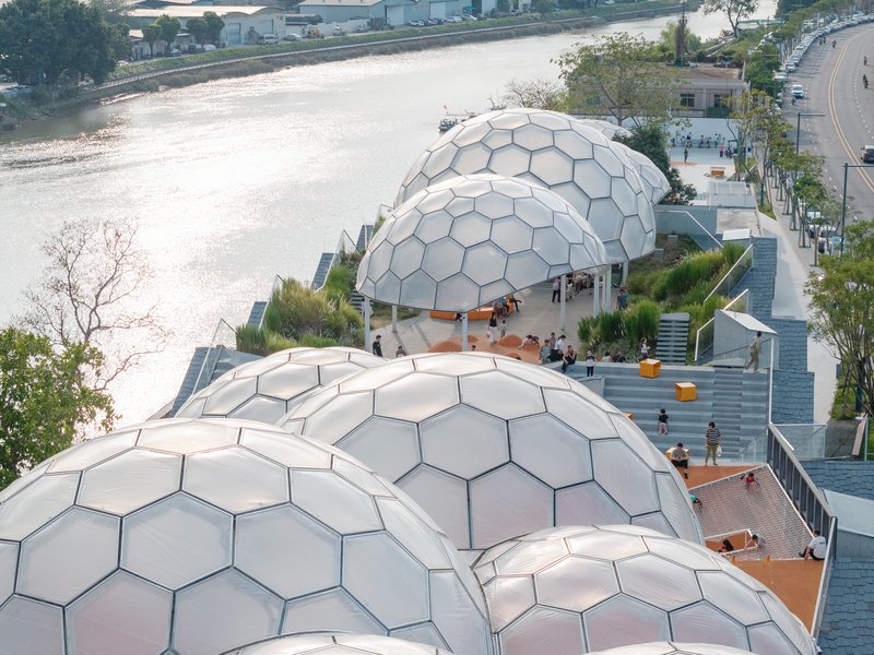 Aerial view of clustered hexagonal dome pavilions along a riverside promenade with visitors on tiered seating