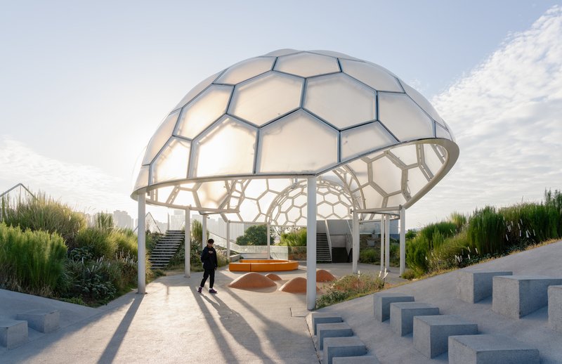 Hexagonal dome pavilion with translucent panels and structural frame casting long shadows at sunset