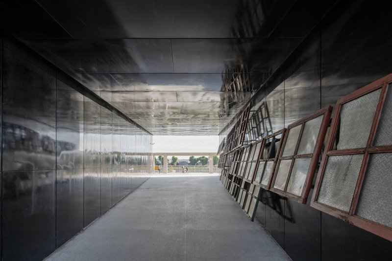 Corridor with reflective metal wall panels and angled wire mesh screens under a polished ceiling