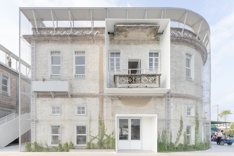 Preserved brick facade enclosed by a new white structural frame with mesh balustrades and climbing vegetation