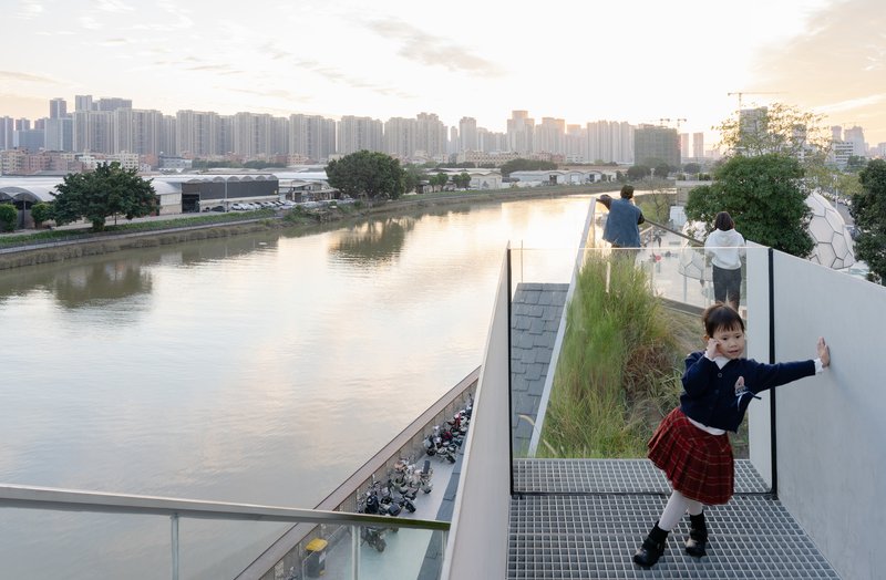 Elevated walkway with planted grasses overlooking the canal at sunset with visitors along the glass balustrade