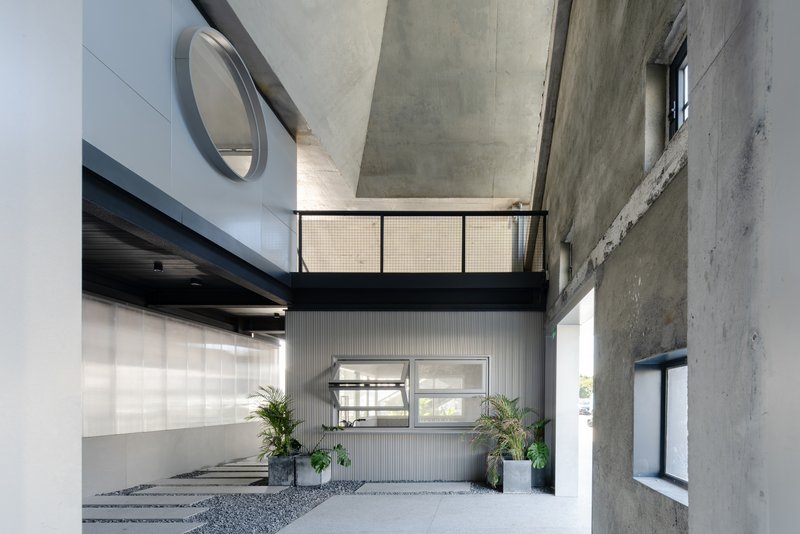 Covered entry courtyard with exposed concrete walls, corrugated metal cladding and potted plants flanking the entrance