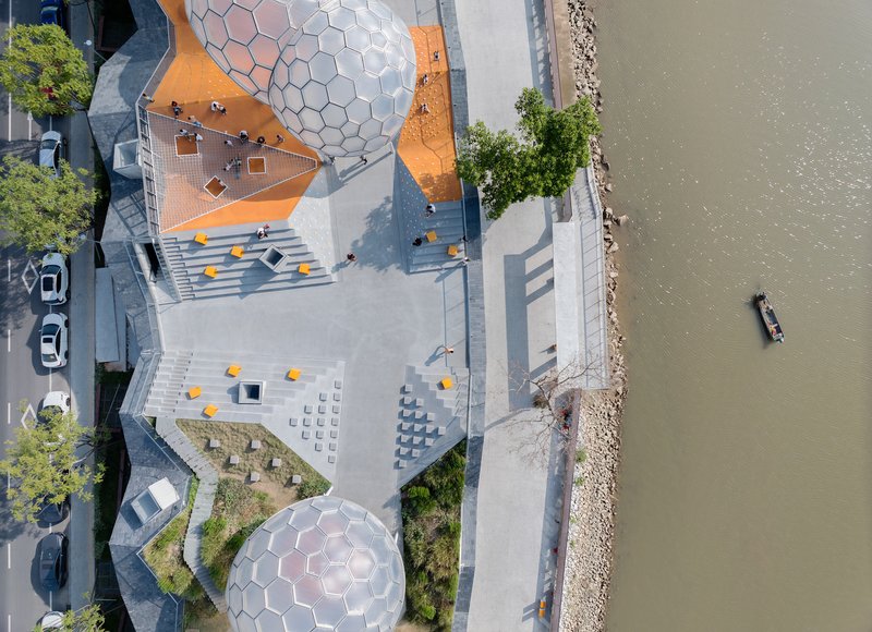 Aerial view of the waterfront plaza with hexagonal dome structures and a boat passing in the river